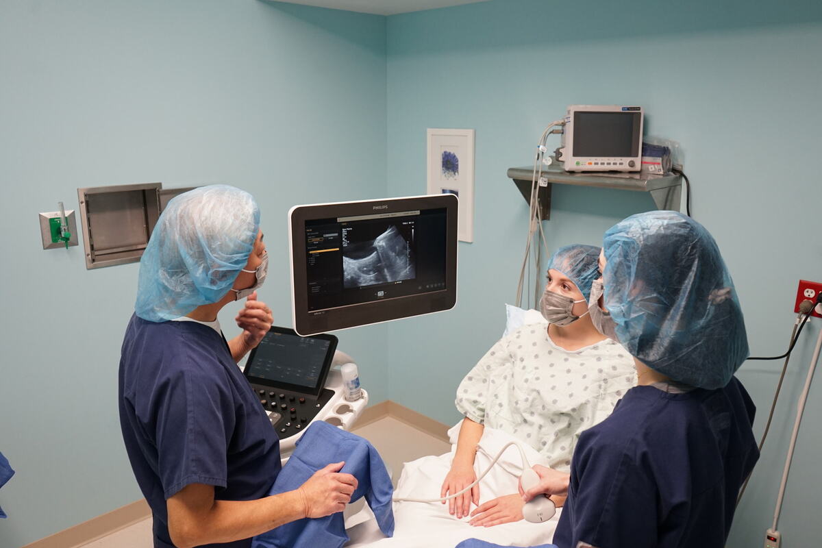 Two individuals wearing scrubs talk to a patient while they look at an ultrasound display