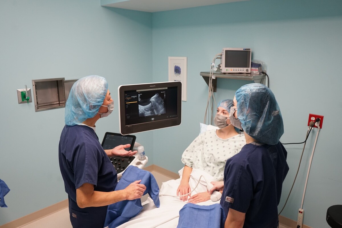 two nurses look talk to a patient while they all look at an ultrasound on a monitor