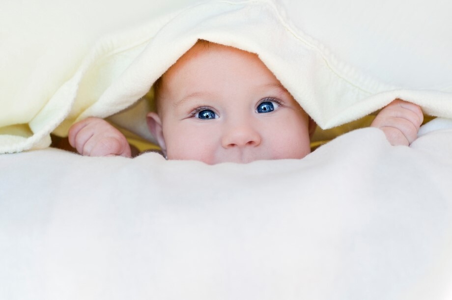 A baby peaks out from underneath a blanket