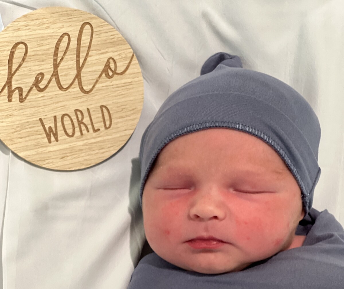 A swaddled new born baby sleeps text reads hello world